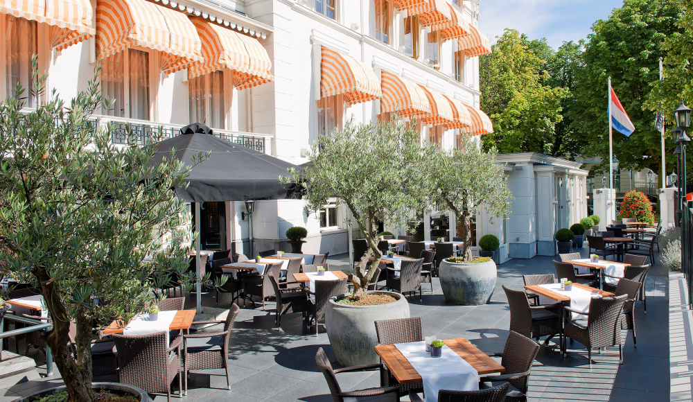 Zonnig hotelterras met bomen, stijlvolle zitplaatsen en oranje luifels Zonnig hotelterras met bomen, stijlvolle zitplaatsen en oranje luifels