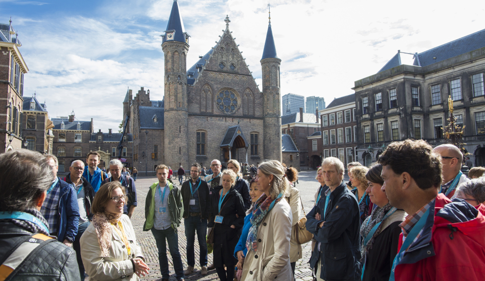 Een groep mensen luisteren naar een gids tijdens een rondleiding over het Binnehof met de Ridderzaal op de achtergrond