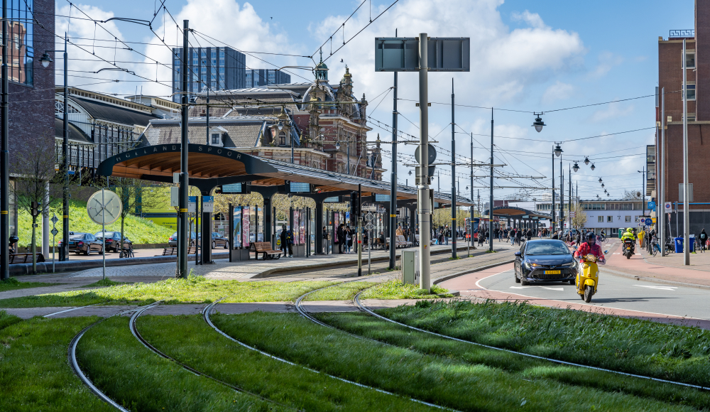 Drukke tramhalte bij het station in Den Haag, met passagiers en voertuigen. (c) Hugo de Wolf