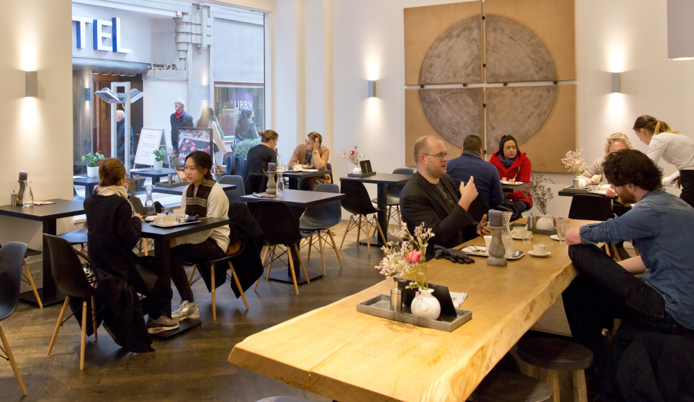 Interieur van Hop & Stork met houten tafels waar mensen koffie aan drinken. 