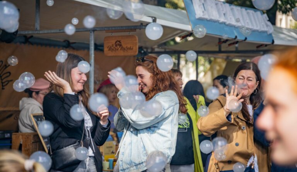 Three women laugh while playing with soap bubbles at a market. (c) Jelle Mes