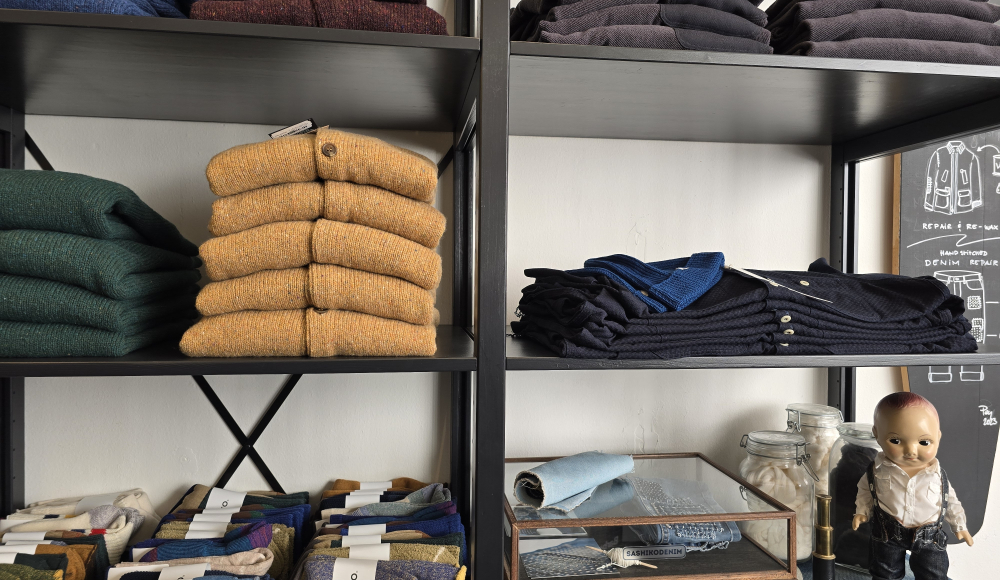 A shelf with stacks of colorful sweaters and knitted accessories.