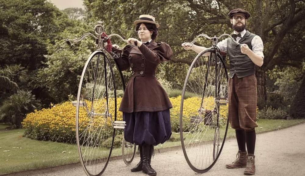 Twee mensen in vintage kleding met hoge ouderwetse fietsen in een park