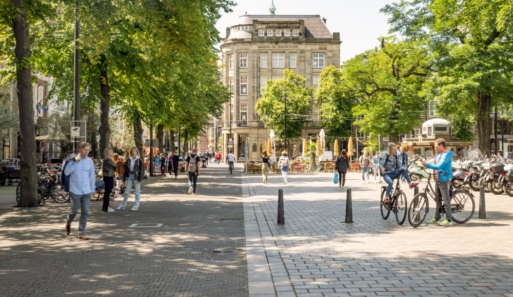 Mensen wandelen en fietsen in een levendige straat met bomen.