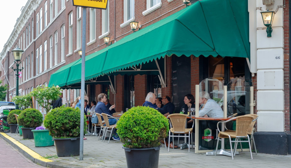 Mensen zitten op een terras met groene parasols in Den Haag.