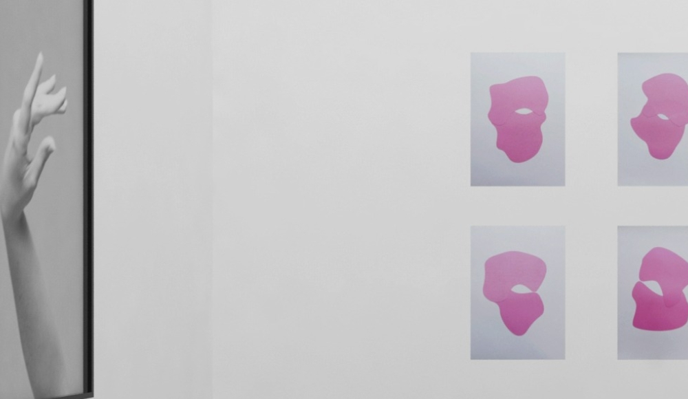 Een foto van een hand in zwart-wit naast vier roze kunstvormen.