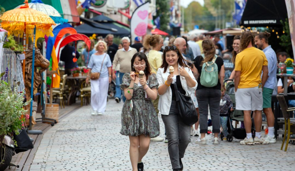 Twee vrouwen lopen met ijsjes in een drukke straat.