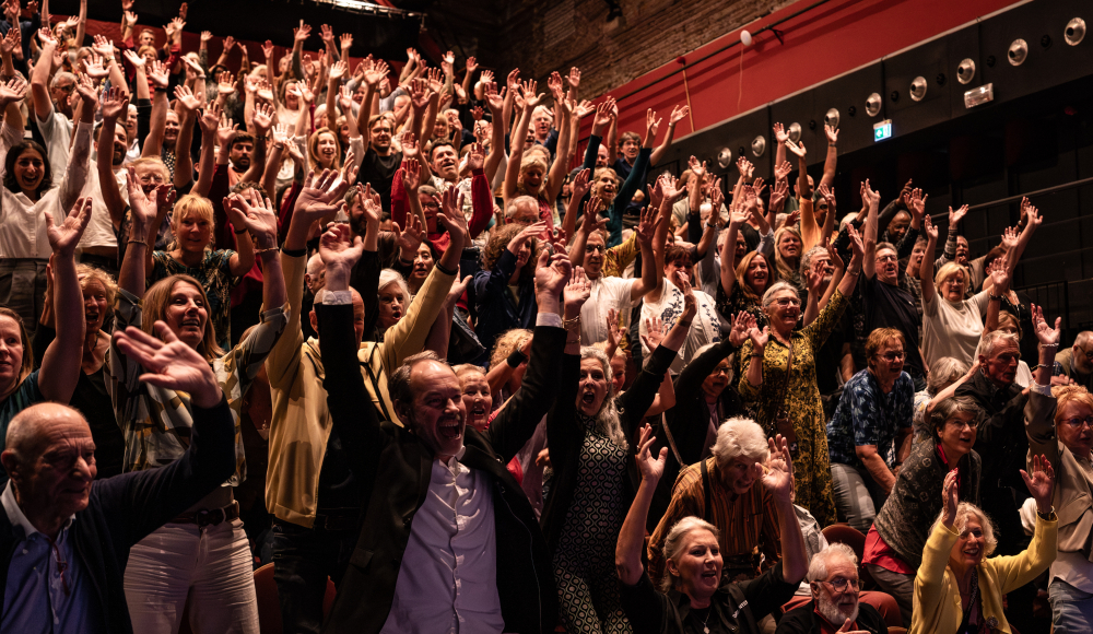 Ein begeistertes Publikum mit erhobenen Händen in Theater De Regentes.