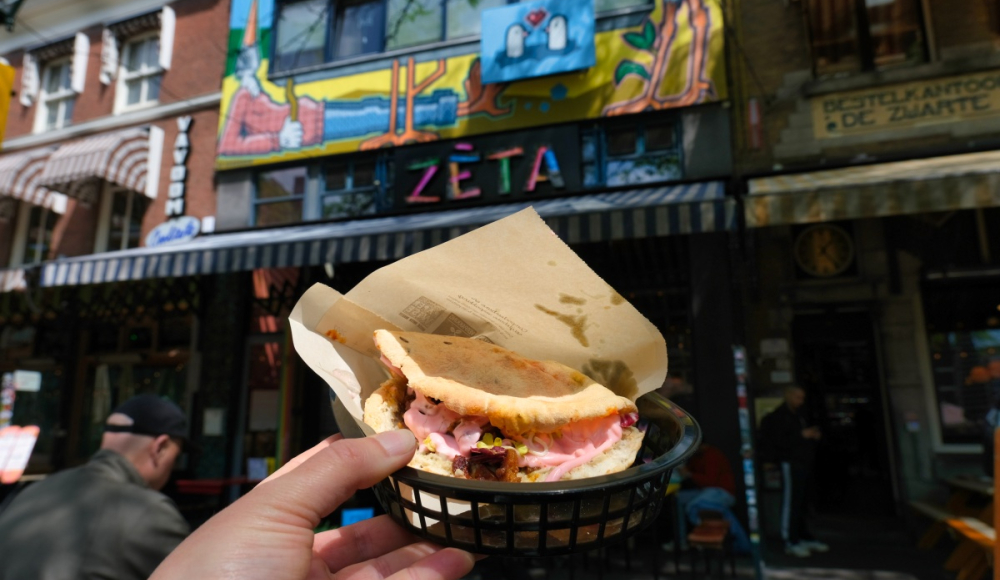 Een hand houdt een sandwich vast voor een kleurrijk restaurant