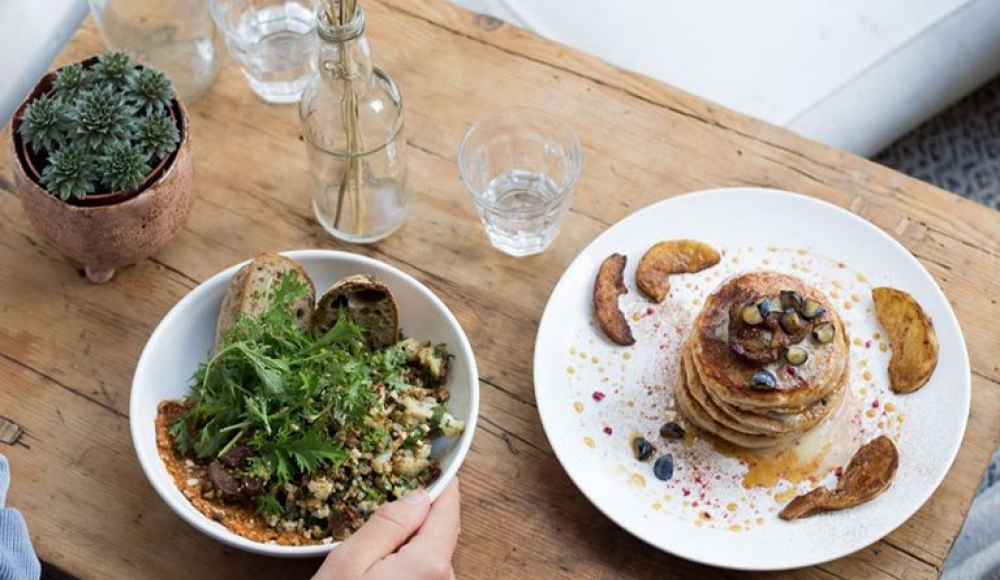 Een tafel in restaurant Plenty met een plantje en droogbloemen waarop een kom sla een boord pancakes staat.