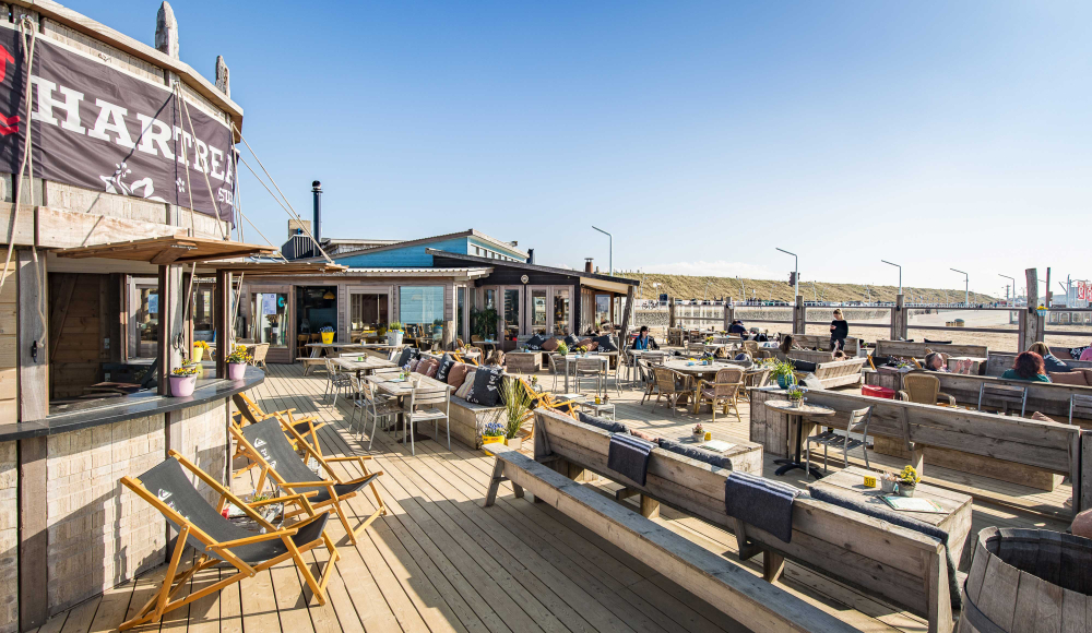 Zonnige terras van Hart Beach met ligstoelen en houten tafels