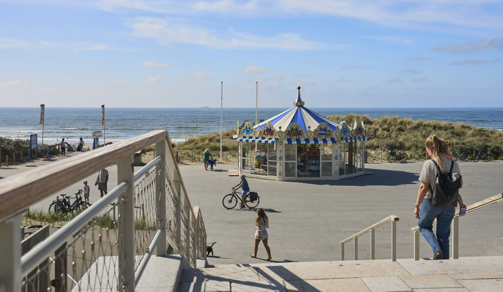 Een kermisattractie bij het strand, fietsers en wandelaars in de buurt.