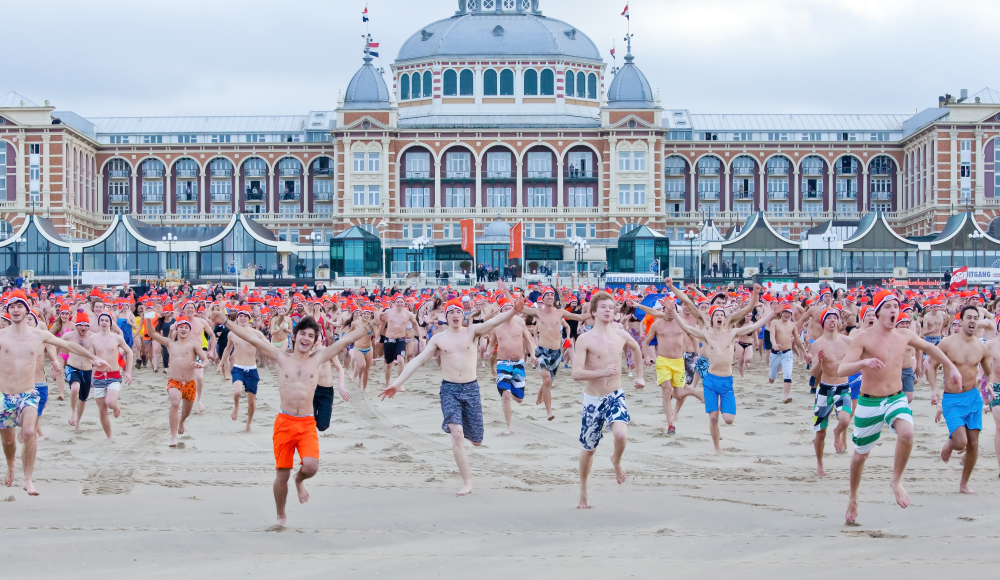 Mensen rennen richting de zee tijdens de Unox Nieuwjaarsduik Scheveningen. Op de achtergrond het Kurhaus