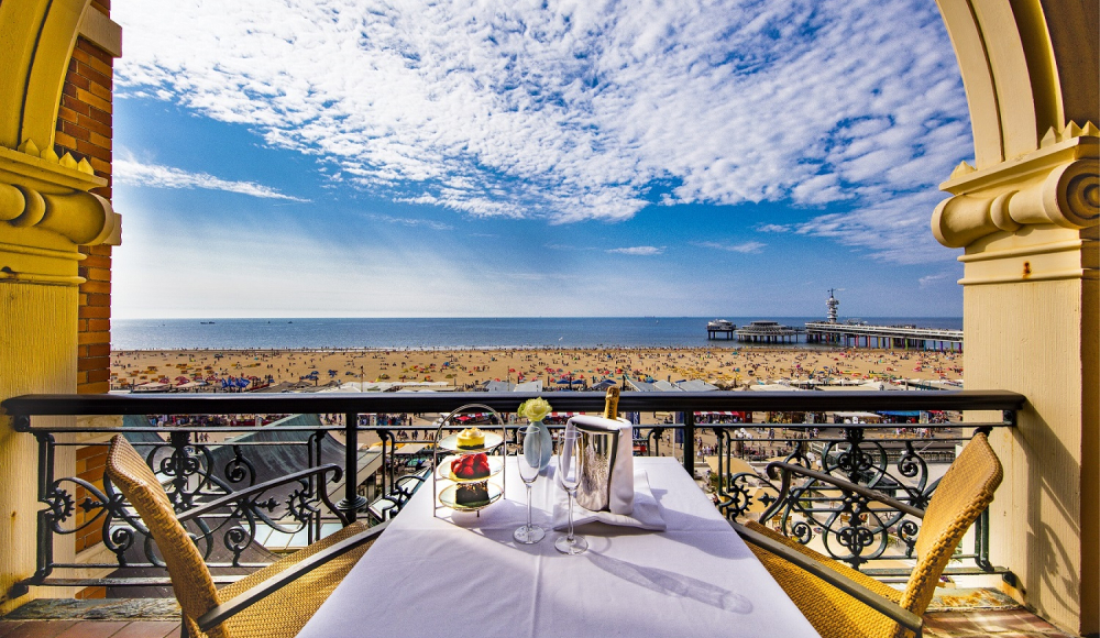 Tafel met macarons en champagne op een balkon met uitzicht op de zee en de Pier van Scheveningen