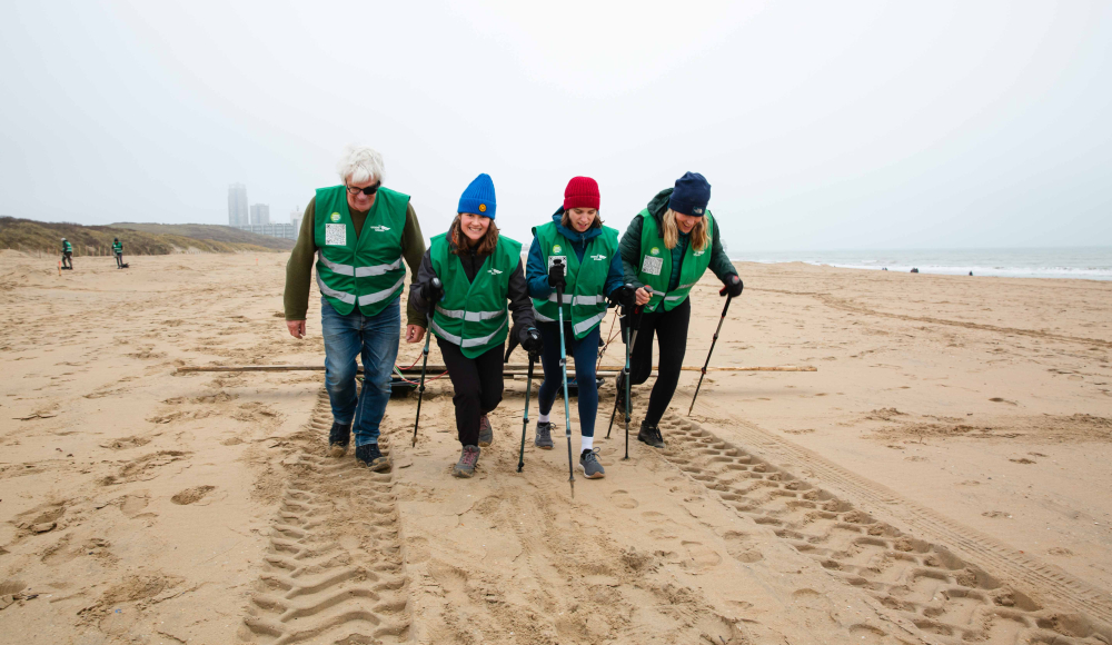 Vrijwilligers met groene vesten wandelen op het strand terwijl ze een slee voorttrekken. (c) Eveline van Egdom