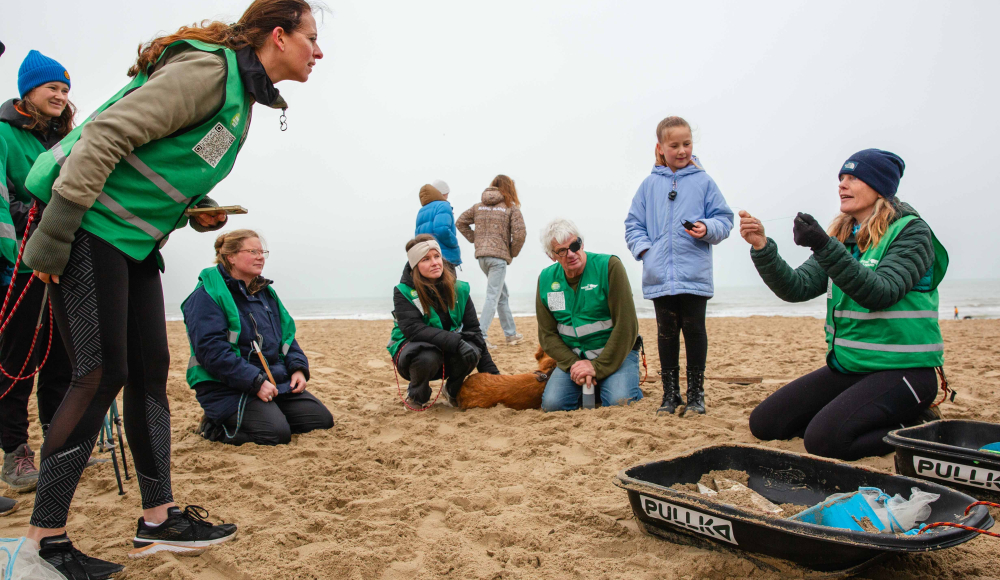 Mensen in groene vesten verzamelen op het strand.