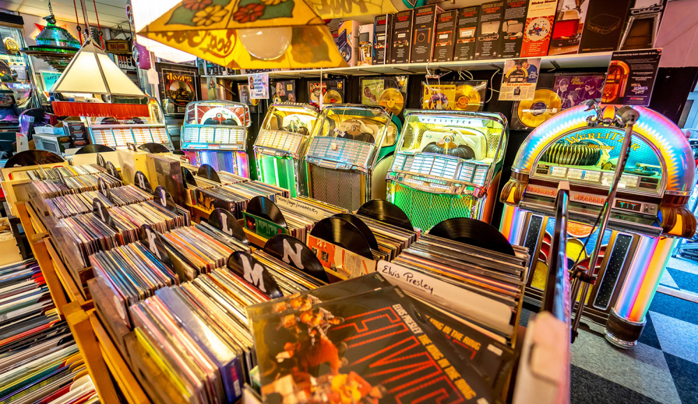 Retro muziek- en platenwinkel met vinylbakken, kleurrijke jukeboxen en vintage muziek, waaronder Elvis Presley-platen en gouden records.