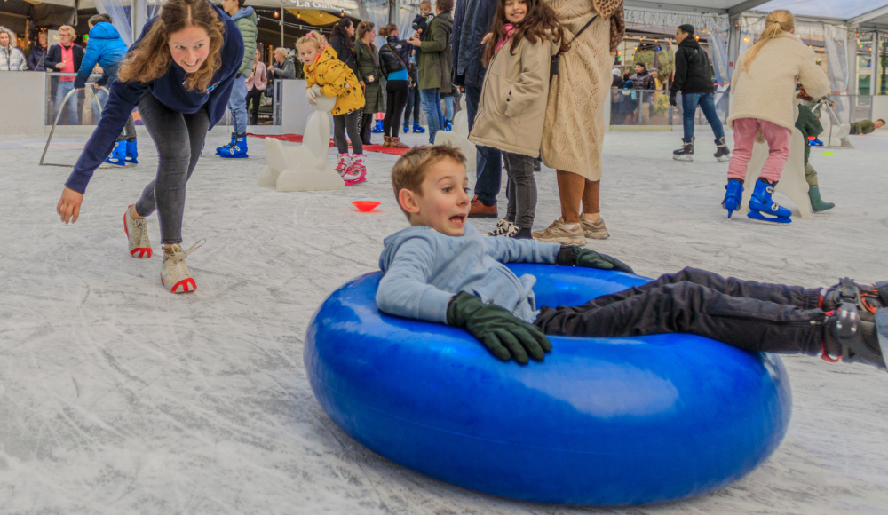 A child slides in a blue ring on the ice rink.