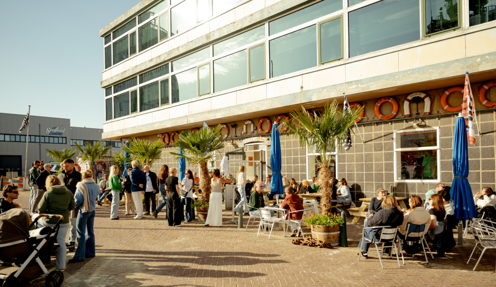 People on a sunny terrace at the Zeemanshuis in the harbour of Scheveningen, surrounded by palm trees and maritime details