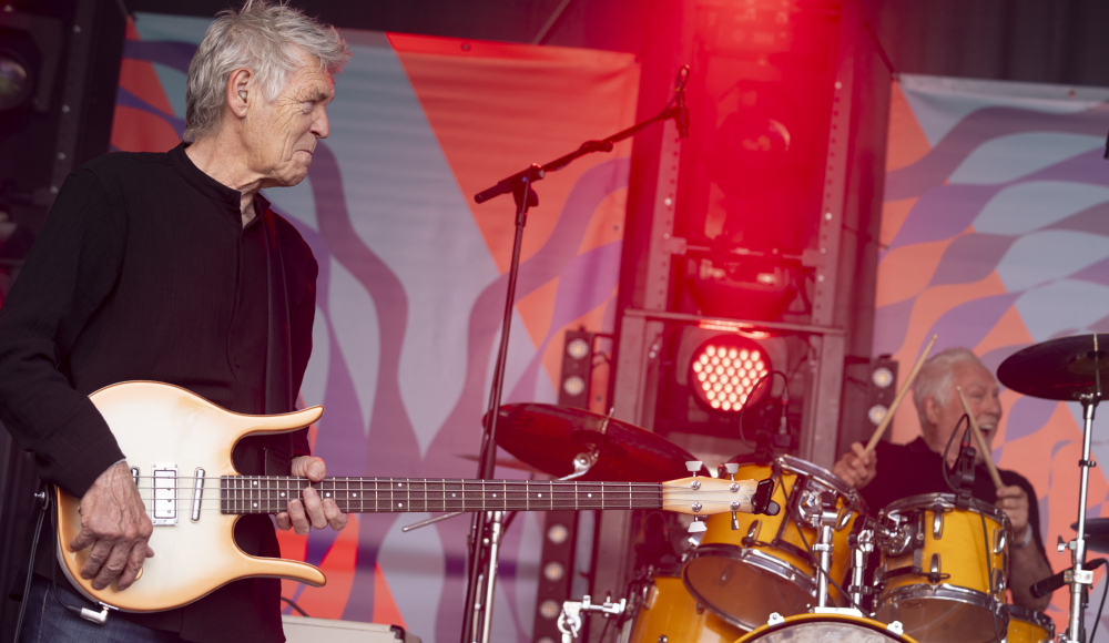 A man playing a bass guitar and a drummer on stage during a performance.