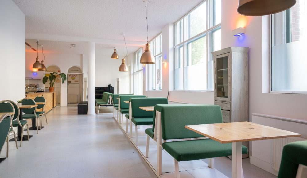 Een lichte, moderne cafésetting met groene stoelen en houten tafels.