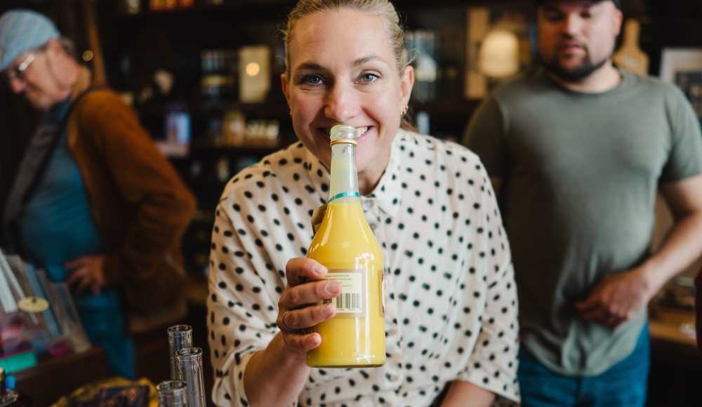 Woman holding a bottle of yellow drink in a store, with others in the background.
