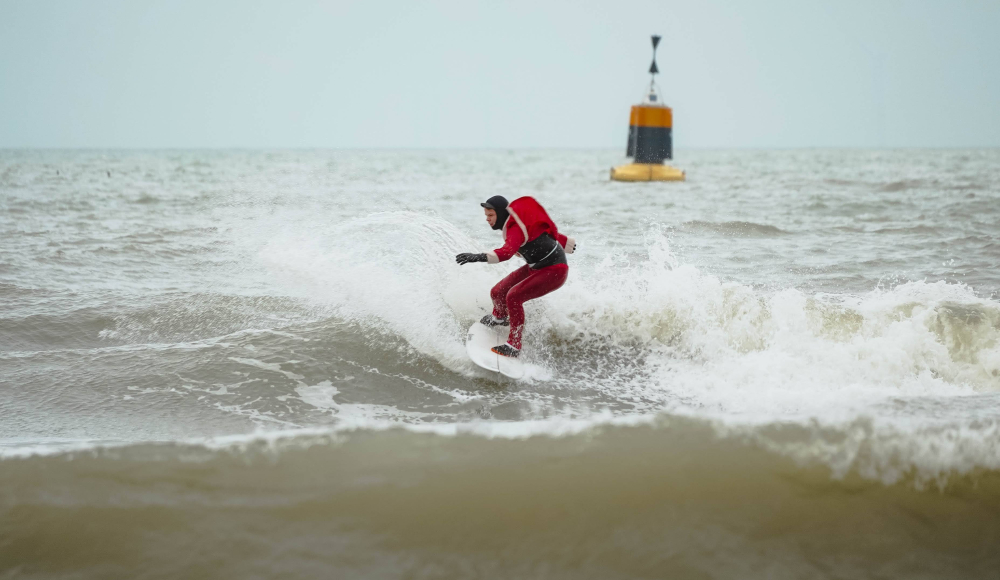 Een surfer in een wetsuit surft op golven voor de kust.
