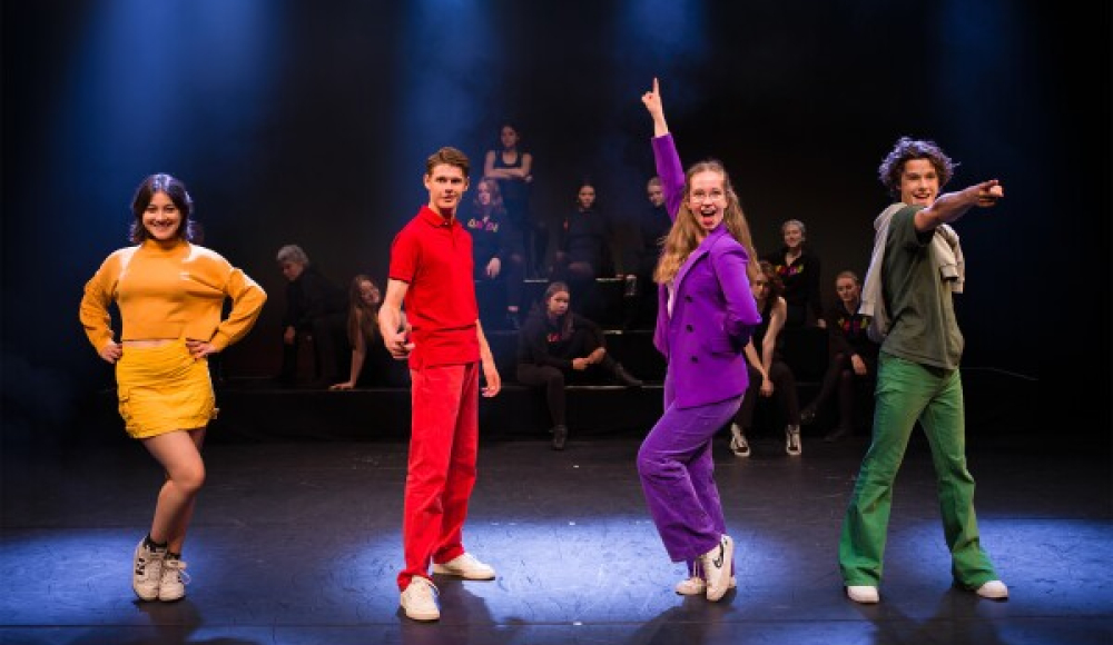 Vijf dansers in kleurrijke kostuums op een podium met spots.