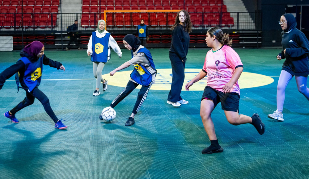 Groep meisjes in sportoutfits spelen voetbal binnen