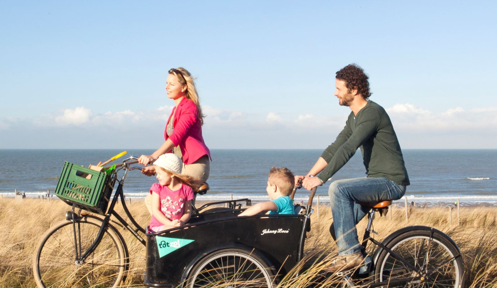 Fietsend stel met kinderen in de bakfiets in de duinen 