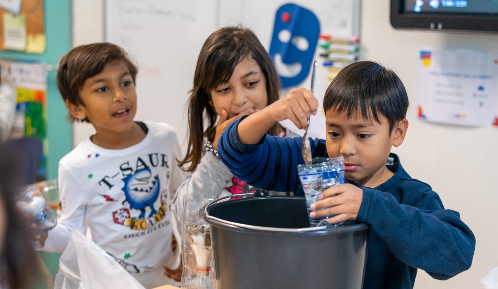 Drie kinderen voeren een waterexperiment uit in de klas.