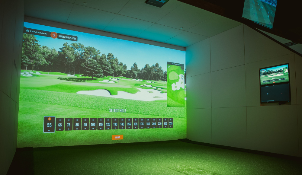 A golf simulator displays a virtual golf course with hole selection.