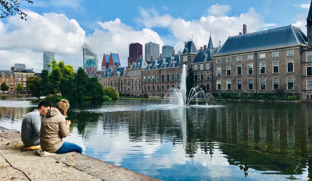 Jongen en meisje eten iets aan de rand van de Hofvijver met hun benen boven het water. 