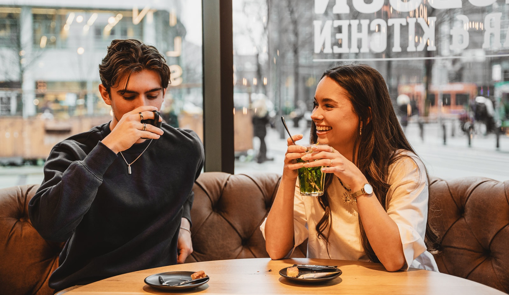Ein Mann und eine Frau sitzen an einem Tisch mit Getränken und lachen.