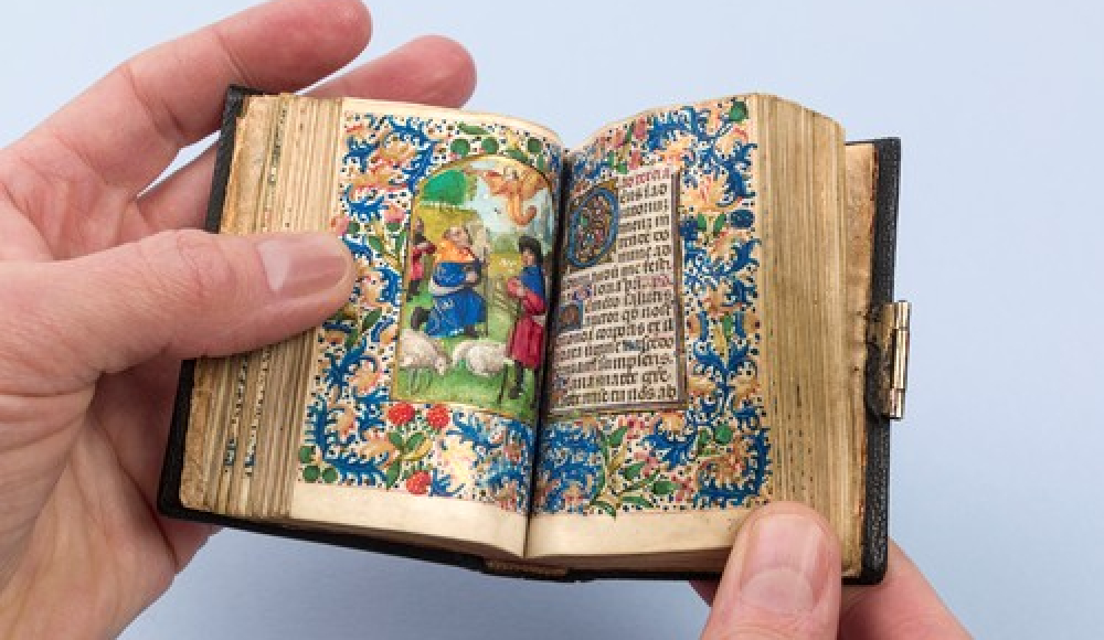Een hand houdt een open, miniatuur bijbel met kleurrijke illustraties. Foto: The Book Photograph