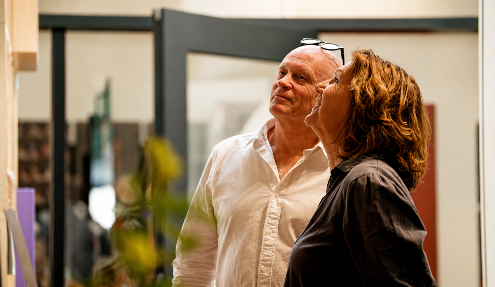 A man and a woman are looking intently at artworks in a gallery.