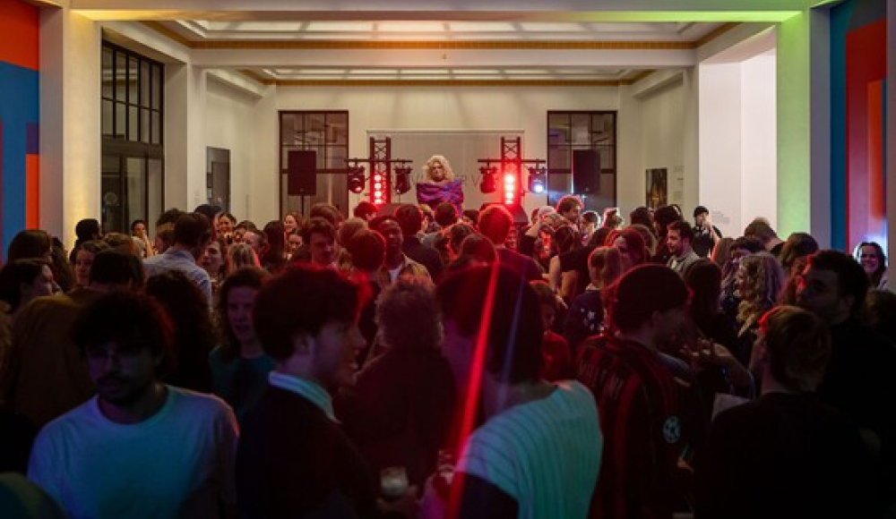 Drukke zaal met mensen tijdens een feest, met kleurrijke verlichting.
