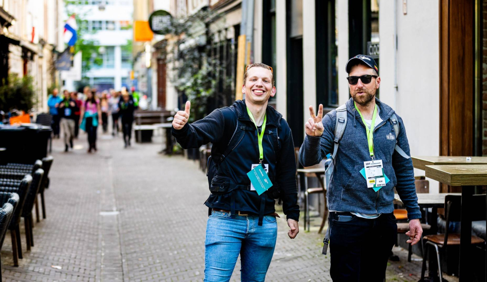 Twee mannen staan in een straat, ze lachen en maken gebaren.