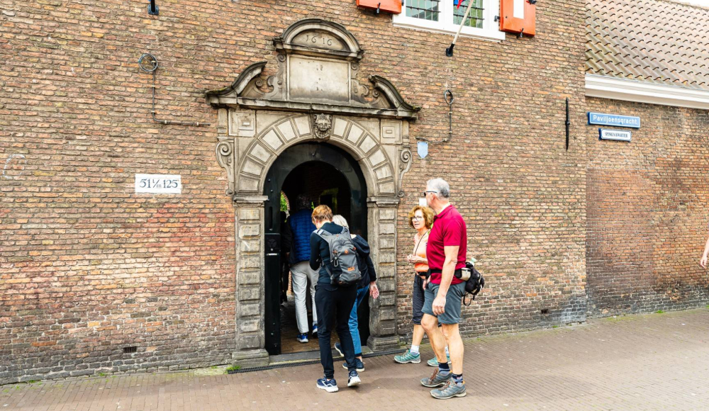 Mensen lopen naar binnen bij de ingang van een oud gebouw in Den Haag.