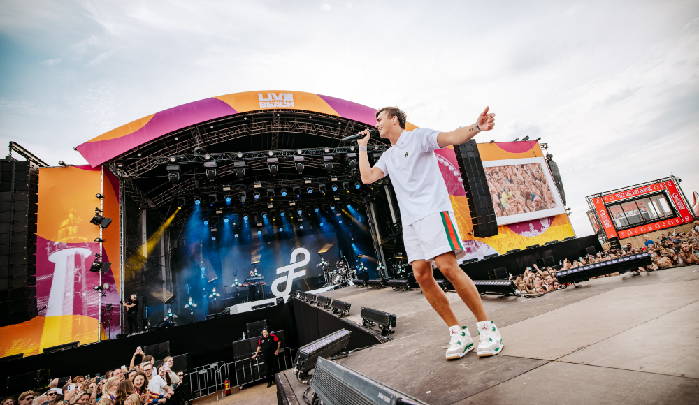 Sänger mit Mikrofon auf der Bühne vor einem Publikum während eines Festivals.