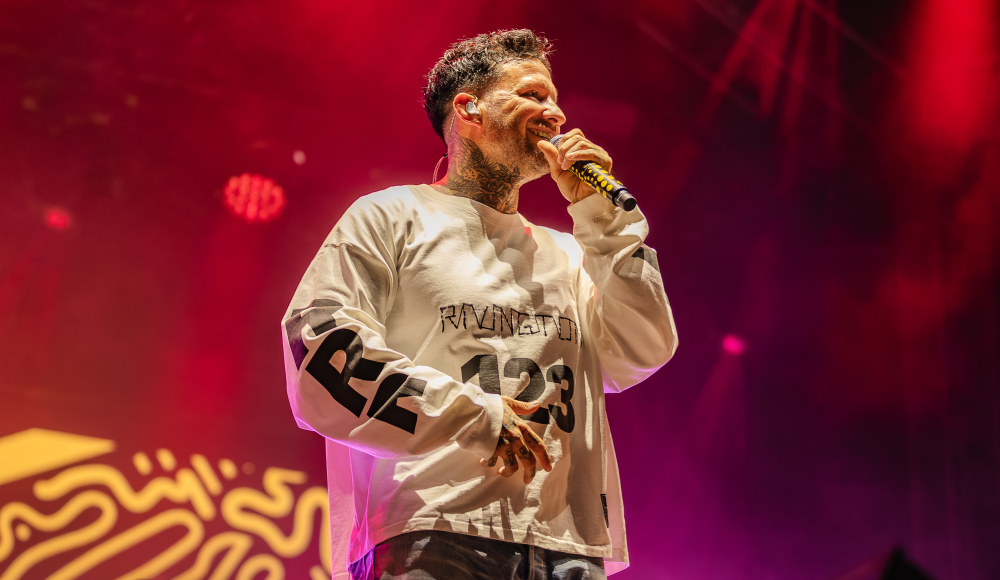 Ein Mann singt auf einer Bühne mit bunten Lichtern.