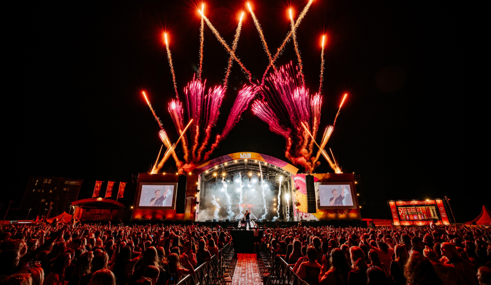 Eine lebendige Nachtaufnahme von einem Musikfestival mit Feuerwerk und großer Bühne.