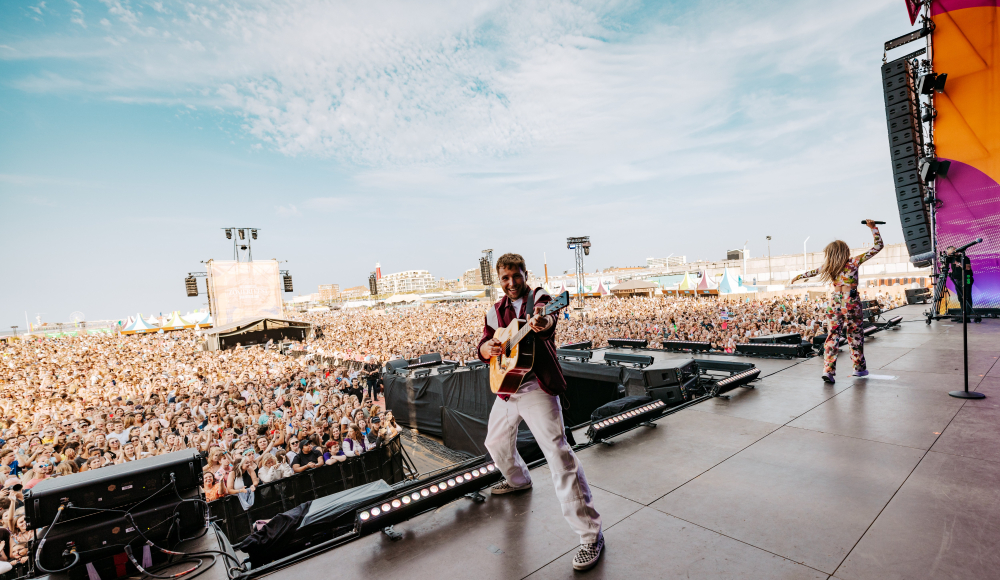 Ein Musiker spielt Gitarre vor einer großen Menge am Strand.