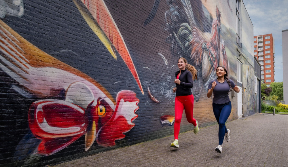 Twee vrouwen joggen langs een gekleurde muurschildering.