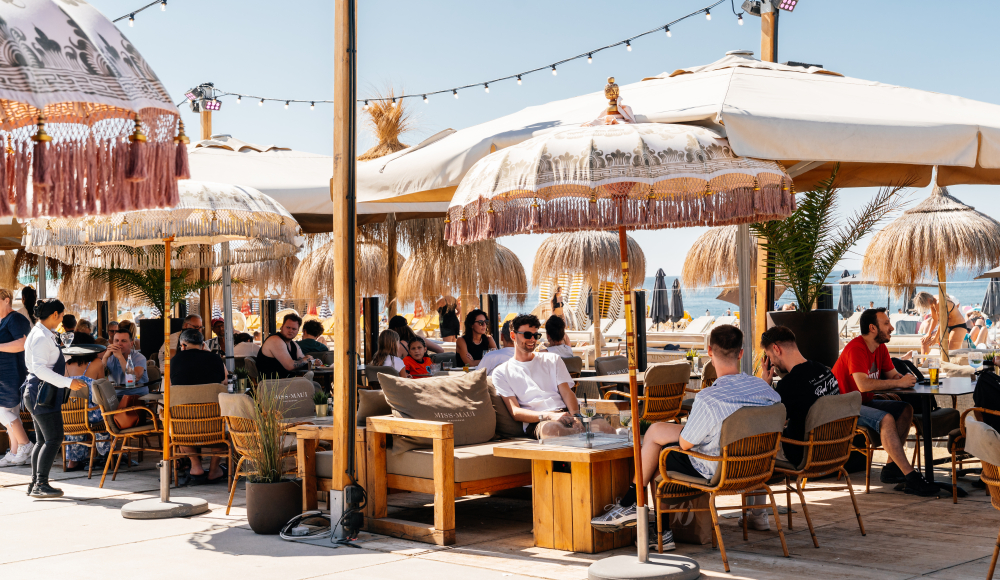 Mensen zitten in een strandtent met parasols in Scheveningen