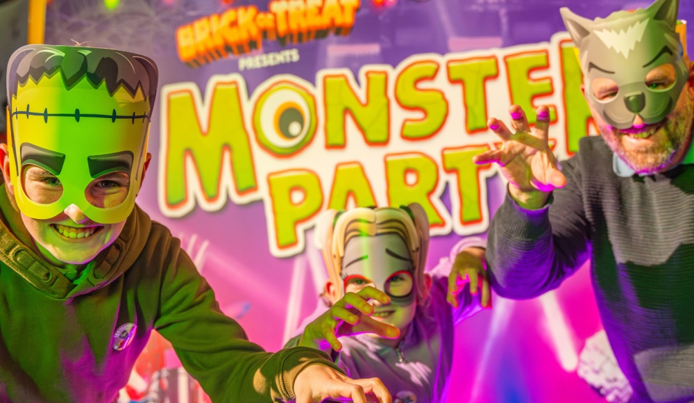 Kinderen en volwassenen met monster maskers voor een banner Monsterparty LEGOLAND®