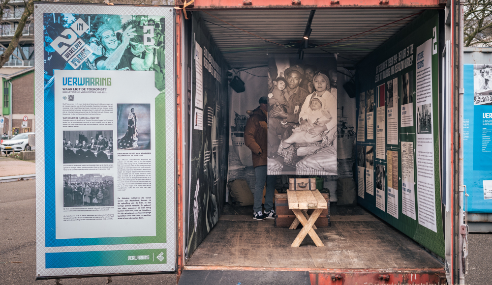 Een man staat in een container met historische foto's en informatiepanelen 75 jaar Molukkers in Nederland. Foto: Ed Leatemia