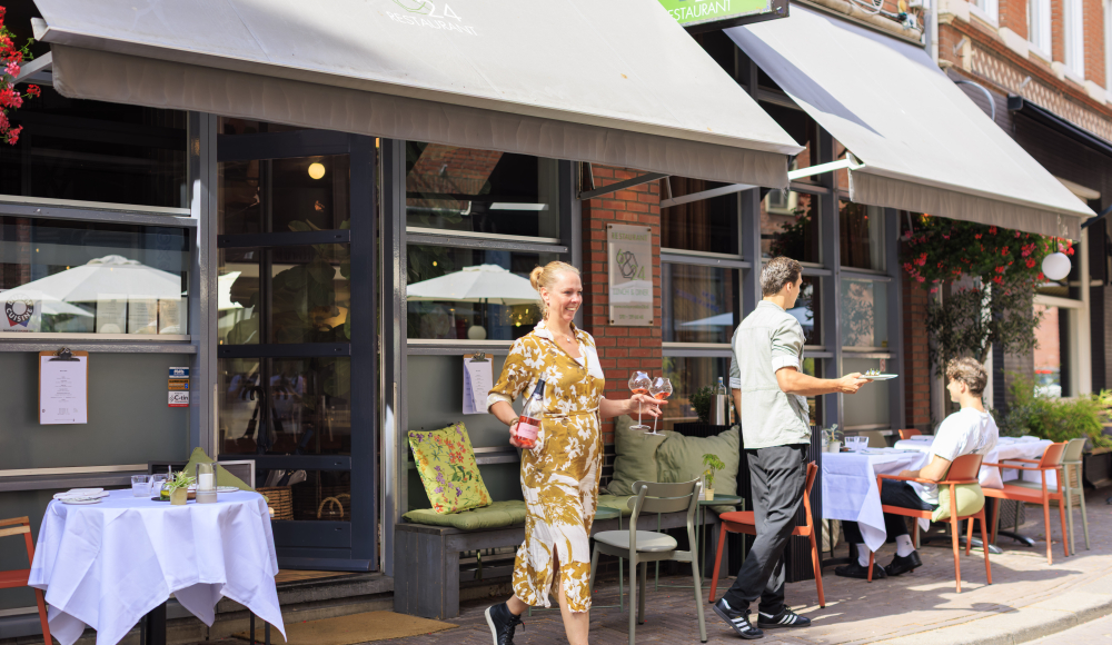 Une femme portant des boissons marche devant un restaurant.