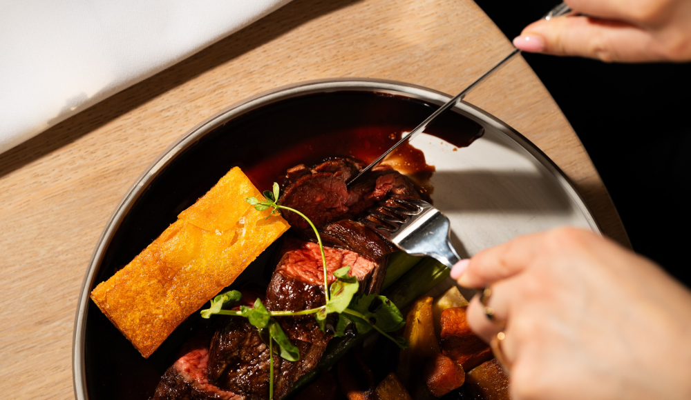 Een persoon snijdt in een steak met groenten en saus.