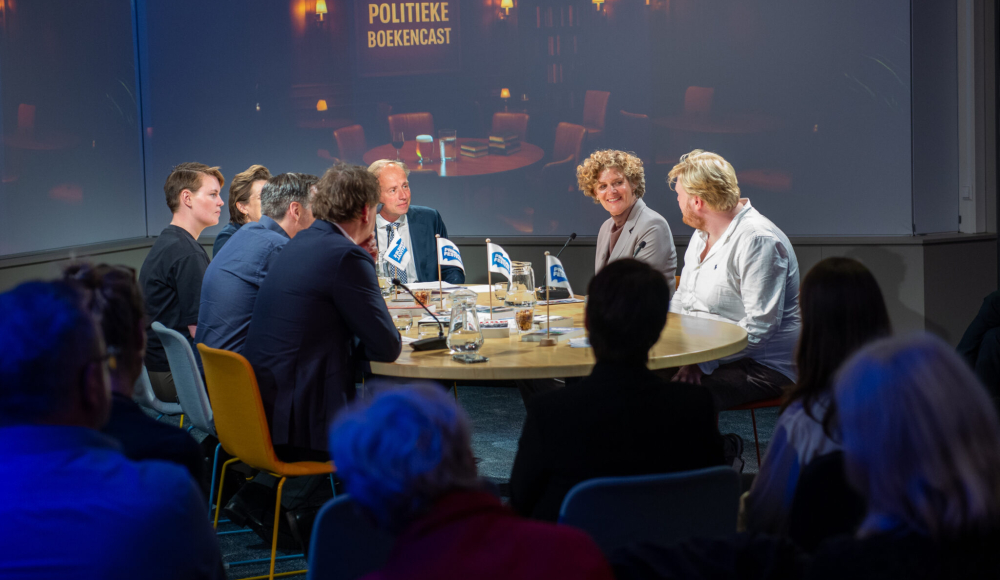 Discussie tussen zes mensen aan een ronde tafel.